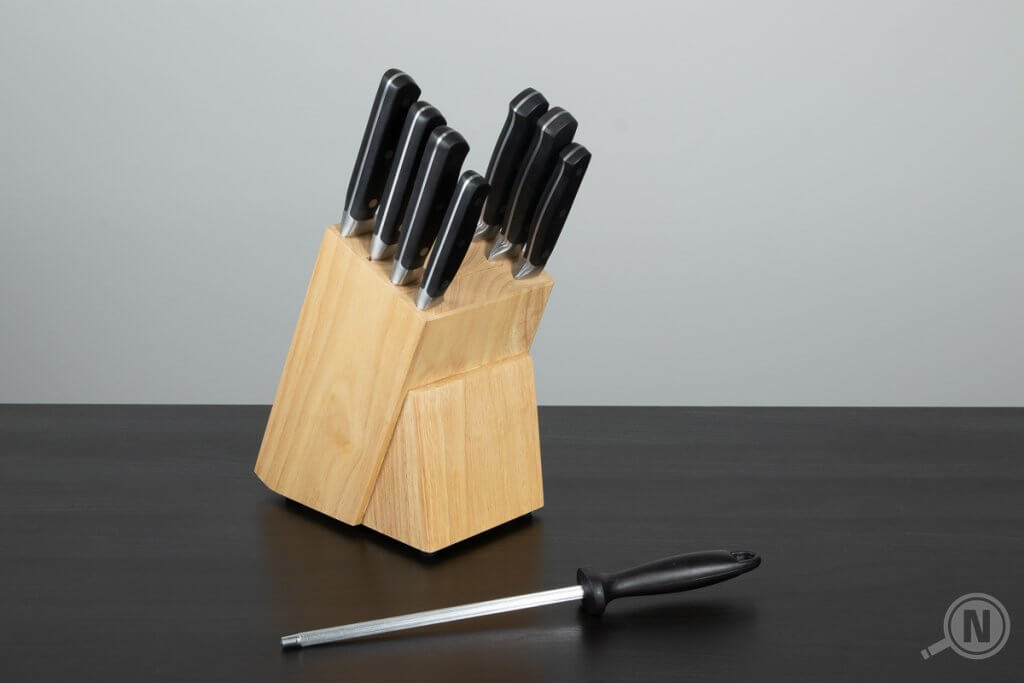 Voll bestückter Messerblock aus Holz auf einem schwarzen Tisch. Ein Wetzstab liegt davor.