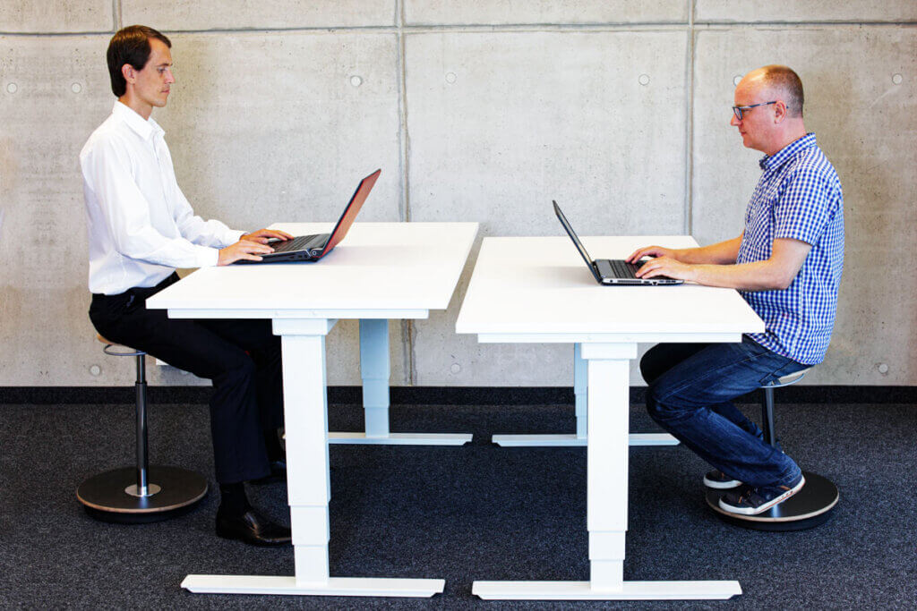 zwei kollegen arbeiten jeweils an einen eigenen hoehenverstellbaren schreibtisch
