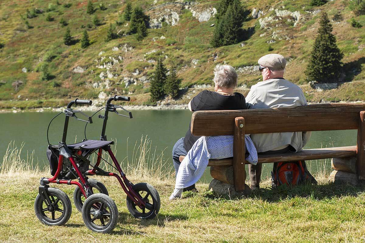 Senioren sitzen auf Bank am See mit Rollator daneben