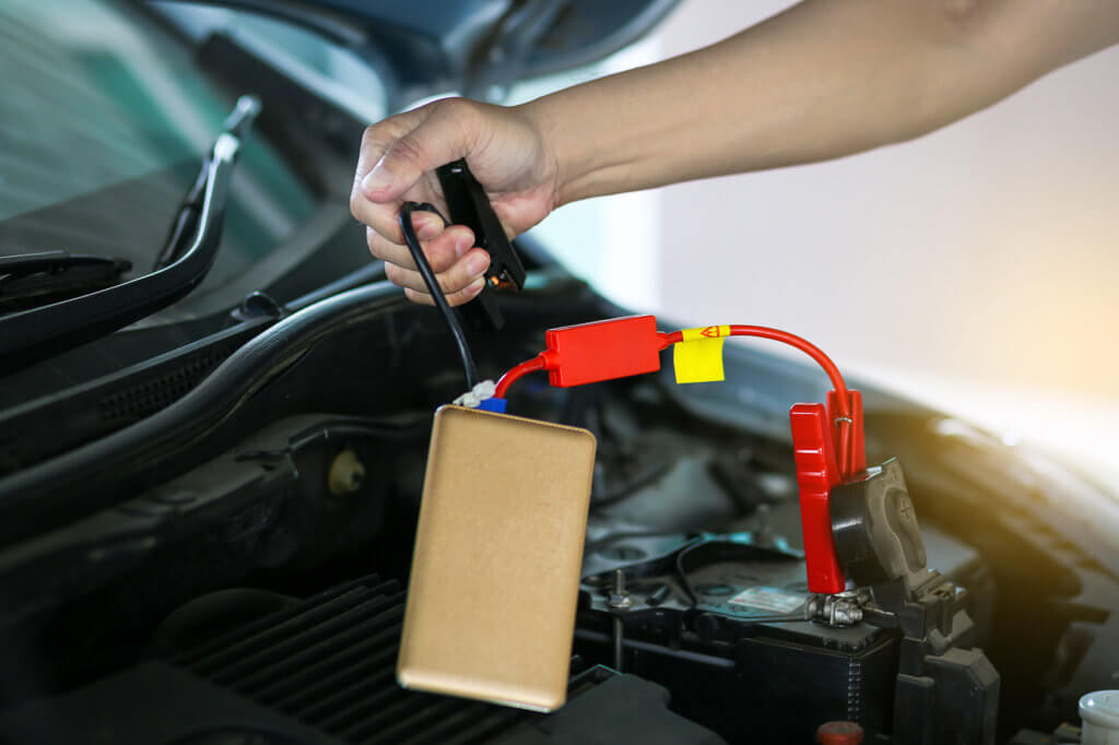 Mann haelt kleines Starthilfegeraetkabel in der Hand